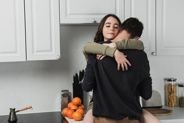 όμορφο νεαρό ζευγάρι αγκαλιάζει σε kithchen κατά τη διάρκεια του πρωινού - Φωτογραφία, εικόνα