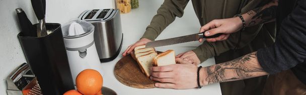 vista cortada do casal preparando café da manhã e cortando pão na cozinha
 - Foto, Imagem