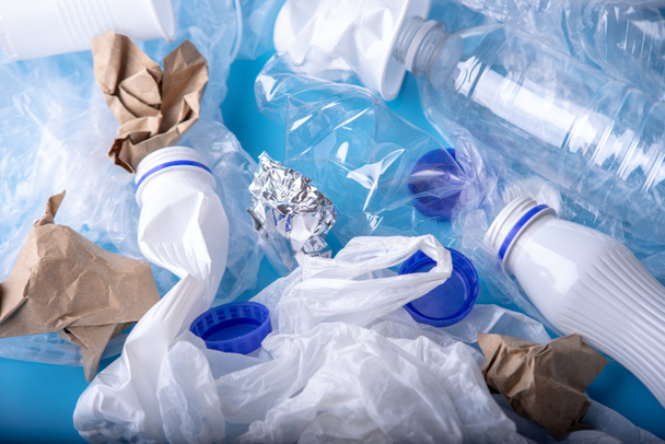 Used unsorted clean garbage in a pile. Bottles, bags and paper on blue background. Concept of environmental pollution and waste sorting - Φωτογραφία, εικόνα