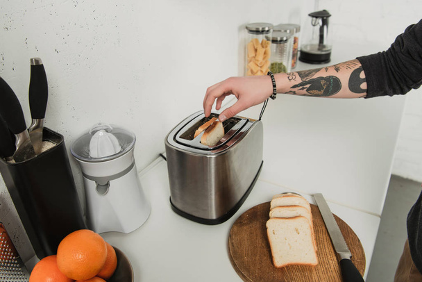 dövmeli adam tost tost makinesiyle kahvaltı sırasında mutfakta hazırlarken görünümünü kırpılmış - Fotoğraf, Görsel