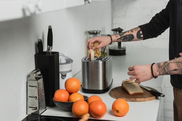обрезанный вид на татуированного человека, готовящего тосты во время завтрака на кухне
 - Фото, изображение
