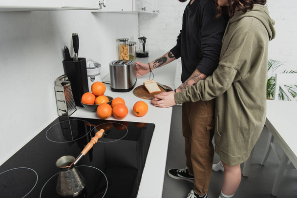 vue partielle du jeune couple préparant des toasts ensemble pendant le petit déjeuner dans la cuisine
 - Photo, image