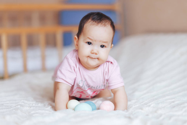 Cute little baby girl, playing with colorful easter eggs in pink clothes, sitting on bed in living room, babygirl smiling happily - Photo, Image