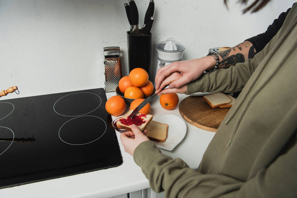 abgeschnittene Ansicht eines Paares, das beim Frühstück in der Küche Toasts mit Marmelade zubereitet - Foto, Bild