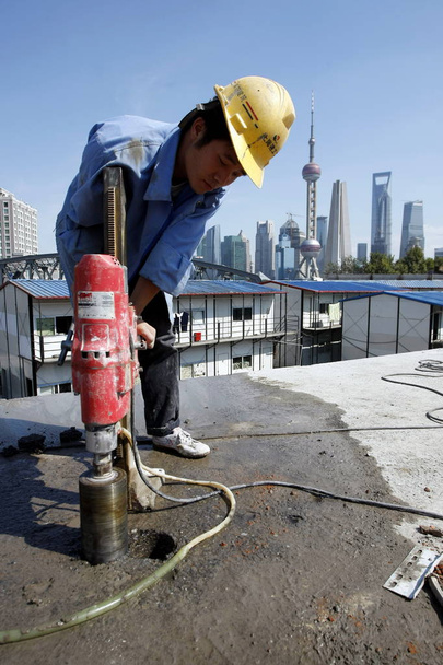 A Chinese construction worker tries to drill a hole in the Wusong Road Bridge over the Suzhou Creek in preparation for the demolition of the bridge as the landscape of the Lujiazui Financial District in Pudong is seen in the background in Shanghai, C - Foto, Bild