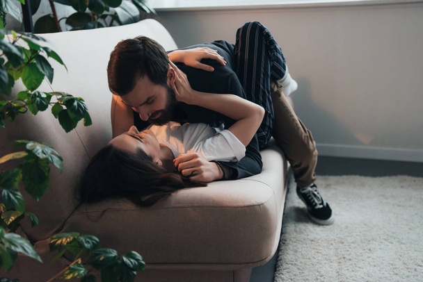 joven pareja apasionada abrazando mientras está acostado en el sofá en casa
 - Foto, imagen