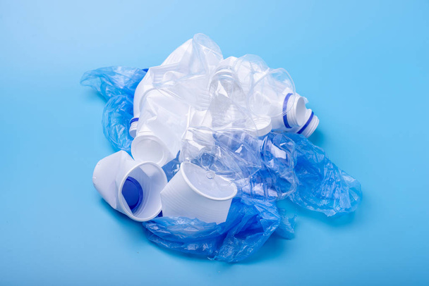 Used plastic garbage in a pile. Bottles and bags on blue background. Concept of environmental pollution and waste sorting - Foto, imagen