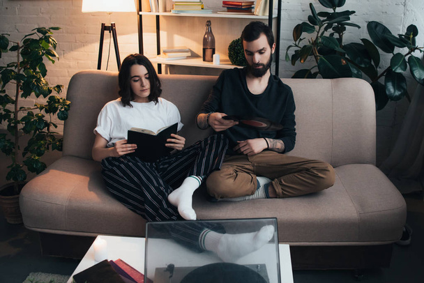 beautiful woman reading book while man holding vinyl record and listening music in living room - Photo, Image