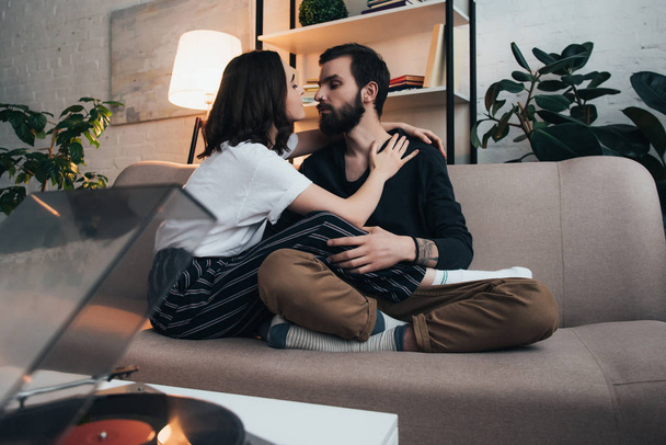 beautiful young couple sitting on couch and listening to vinyl record in living room - Photo, Image