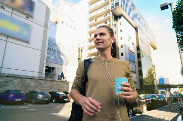 Stylish tall young man (hipster) is standing on the street of a big noisy city and drinking coffee. Life in the metropolis. Food on the go - Φωτογραφία, εικόνα