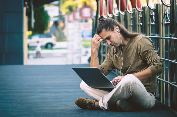 Стильный молодой хипстер, сидящий на ступеньках торгового центра с ноутбуком
 - Фото, изображение