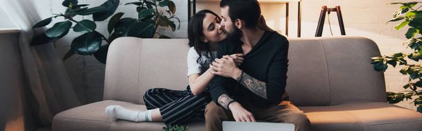 hermosa joven tatuado pareja abrazando mientras sentado en sofá en sala de estar
 - Foto, imagen