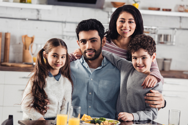 fröhliche hispanische Familie lächelt, während sie zu Hause in die Kamera schaut - Foto, Bild