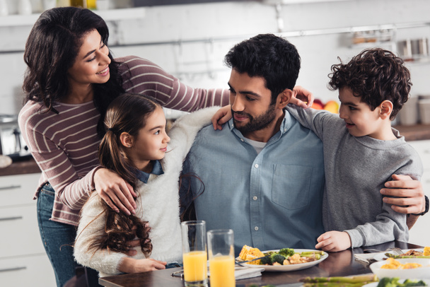 cheerful hispanic family smiling while hugging near lunch at home - Foto, imagen