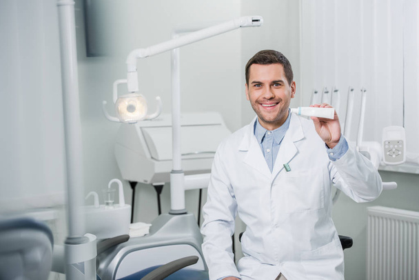 Veselý zubař držící zubní pasta s úsměvem v zubní klinice - Fotografie, Obrázek