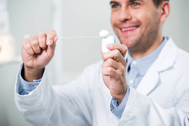 selective focus of dental floss in hands of smiling dentist - Foto, afbeelding