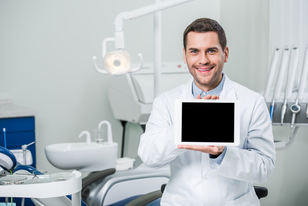 alegre dentista de capa blanca sosteniendo tableta digital con pantalla en blanco
 - Foto, Imagen