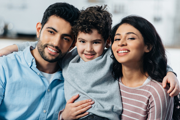 ευτυχισμένη οικογένεια Λατινική αγκάλιασμα κοιτάζοντας την κάμερα στο σπίτι - Φωτογραφία, εικόνα