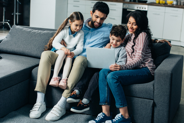 happy hispanic family sitting on sofa and looking at laptop at home - Photo, Image