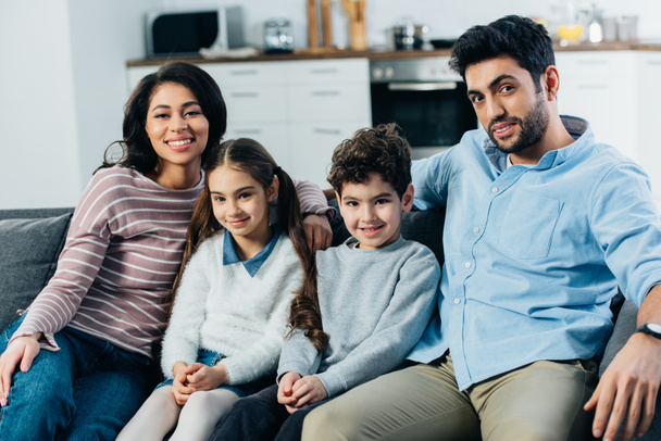 ευτυχισμένος Ισπανόφωνος οικογένεια κάθεται στον καναπέ και να χαμογελά στο σπίτι - Φωτογραφία, εικόνα