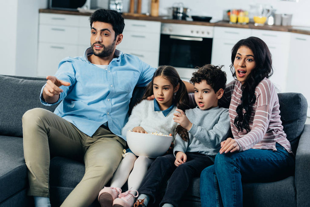 hombre latino señalando con el dedo mientras ve la televisión con la familia hispana en casa
 - Foto, imagen