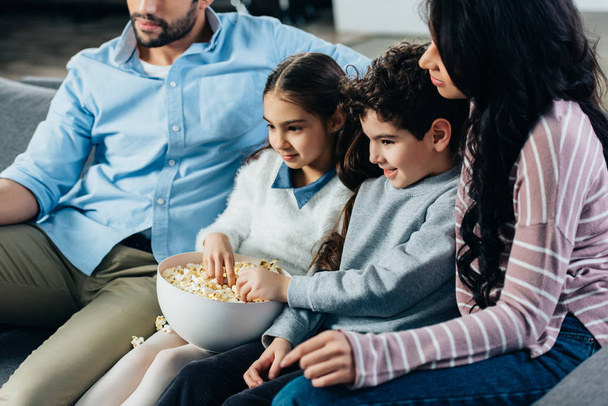cheerful hispanic family watching tv with popcorn bowl at home - Foto, imagen