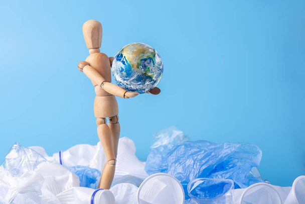 木製のおもちゃの形の人間は、ゴミやプラスチックから地球を救うために手に地球を運びます。廃棄物リサイクルエンドエコロジーの概念ナサが提供する要素 - 写真・画像