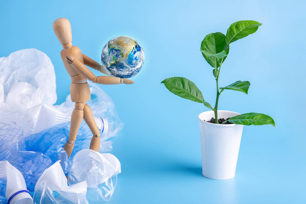 Menschen in Form von Holzspielzeug tragen den Planeten in den Händen zu grünen Pflanzen, um die Erde vor Müll und Plastik zu retten. Ökologie und Abfallrecycling. Elemente von nasa - Foto, Bild