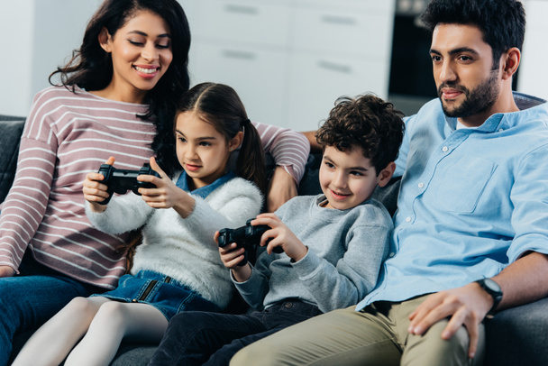 自宅でビデオ ゲームを遊んでいる子供の近くのソファに座っている陽気な親 - 写真・画像