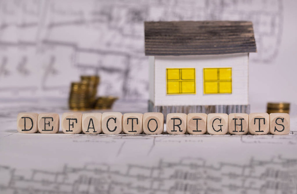 Mots DE FACTO DROITS composés de lettre en bois. Petite maison en papier en arrière-plan. Gros plan
 - Photo, image