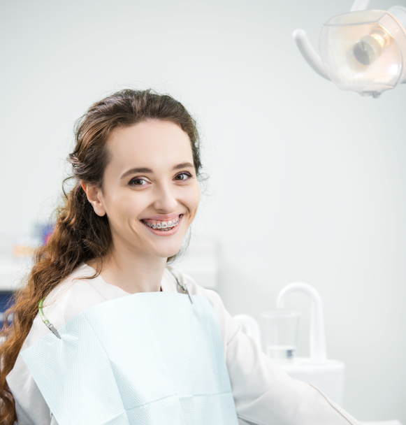 веселая женщина с брекетами на зубах, улыбающаяся в стоматологической клинике
 - Фото, изображение