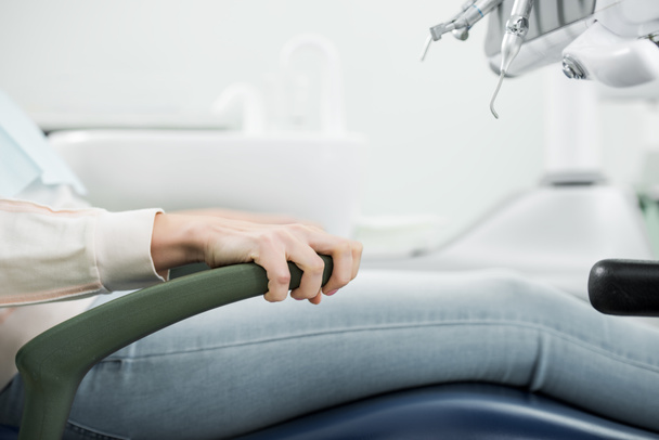 περικοπεί θέα θηλυκός ασθενής που κατέχουν λαβή καρέκλα σε οδοντιατρείο - Φωτογραφία, εικόνα