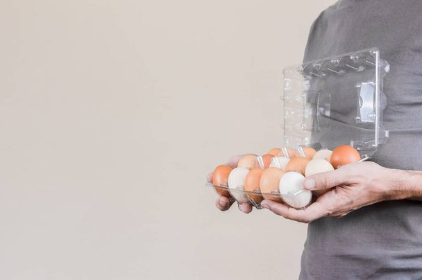 Kaukaski mężczyzna z szary tshirt trzymając jajko plastikowe pudełko pełne jaj kurzych. - Zdjęcie, obraz
