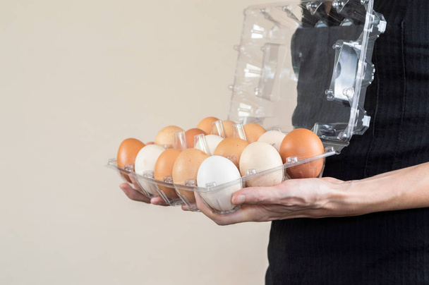Kaukaski kobieta z czarną koszulę trzymając jajko plastikowe pudełko pełne jaj kurzych. - Zdjęcie, obraz