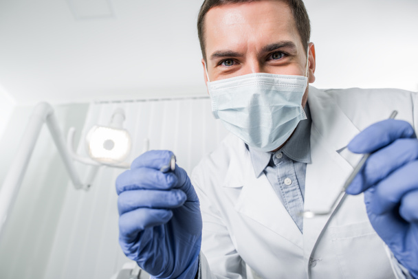 selective focus of dentist in latex gloves and mask holding dental instruments in hands - Photo, Image