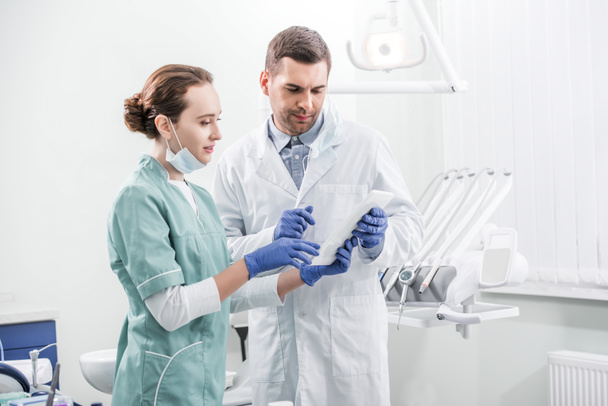 стоматологи, стоящие и глядя на цифровые таблетки в стоматологической клинике
 - Фото, изображение