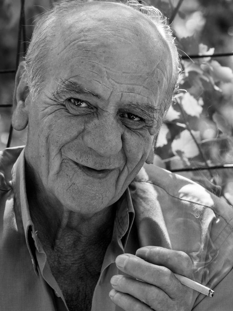 Siyah beyaz bir gülümseme ile bir sigara içen bir ciddi eski Yunan emekli erkek portre portre - Fotoğraf, Görsel