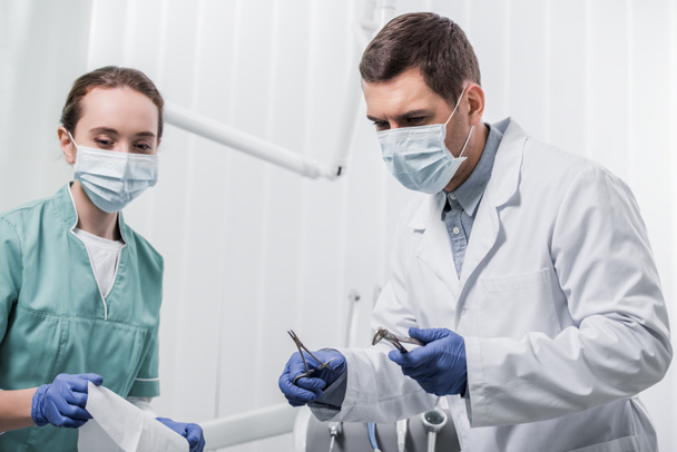 dentista femenina de pie cerca de colega en máscara con instrumentos dentales
  - Foto, Imagen