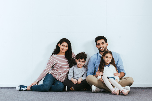 щаслива іспаномовна сім'я сидить на підлозі біля білої стіни
  - Фото, зображення