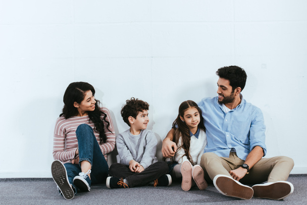 χαρούμενα Ισπανόφωνος οικογένεια κάθεται στο πάτωμα κοντά στο λευκό τοίχο  - Φωτογραφία, εικόνα
