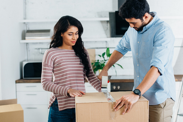 happy latin couple packing boxes while moving to new home - Foto, imagen