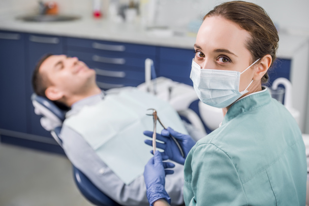 enfoque selectivo del dentista femenino en la máscara que sostiene el instrumento dental cerca del paciente
  - Foto, Imagen