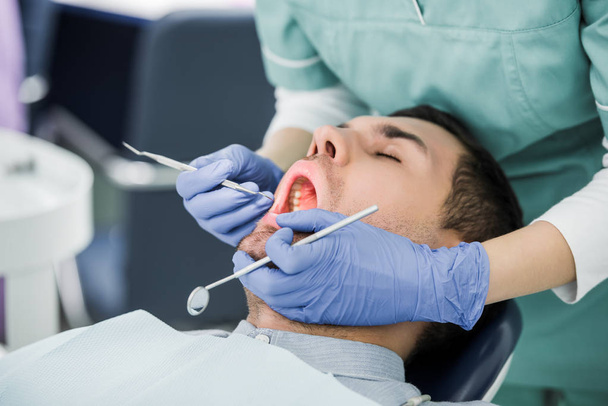 vista recortada del dentista femenino en guantes de látex examinando al paciente con la boca abierta
 - Foto, Imagen