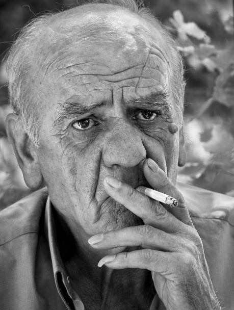 Portrait rapproché d'un vieil homme grec à la retraite qui fume une cigarette avec un sourire, en noir et blanc
 - Photo, image