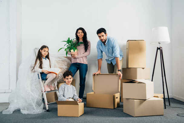 cheerful latin family standing near boxes while moving into new home - Photo, Image