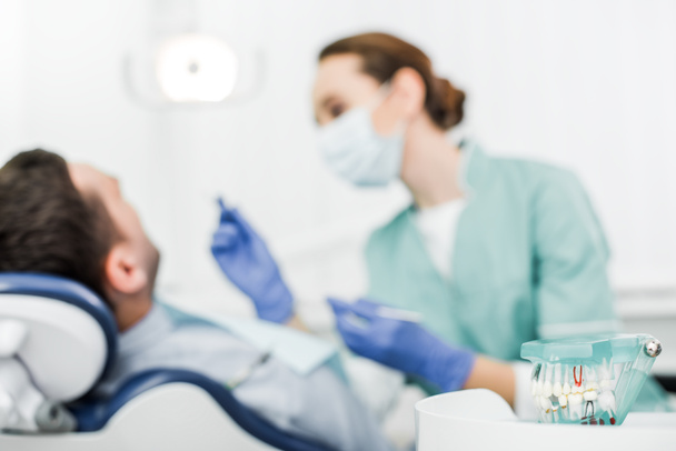selective focus of teeth model near patient and dentist in mask with dental instruments  - Photo, Image