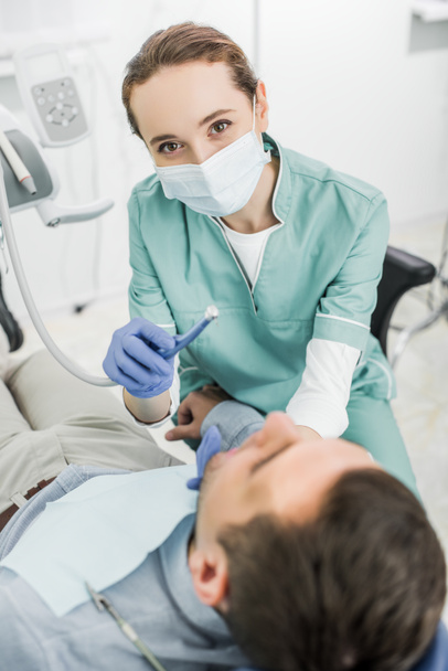 Kobieta dentysty w maskę przytrzymując dentystyczny wiertło podczas pracy z pacjentem w klinice stomatologicznej - Zdjęcie, obraz