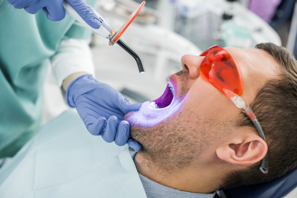 vista ritagliata del dentista rendendo procedura di sbiancamento al paziente in occhiali
 - Foto, immagini