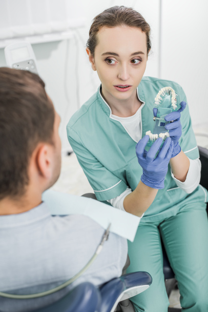 enfoque selectivo del hermoso dentista que sostiene el modelo de dientes cerca del paciente
 - Foto, Imagen