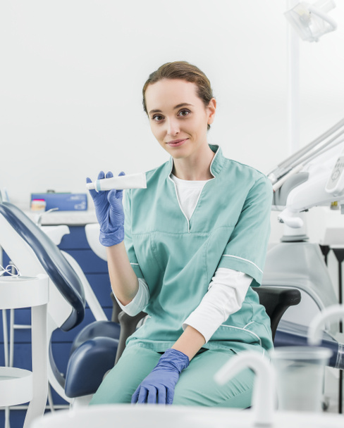 selective focus of cheerful female dentist holding toothpaste  - Foto, Bild